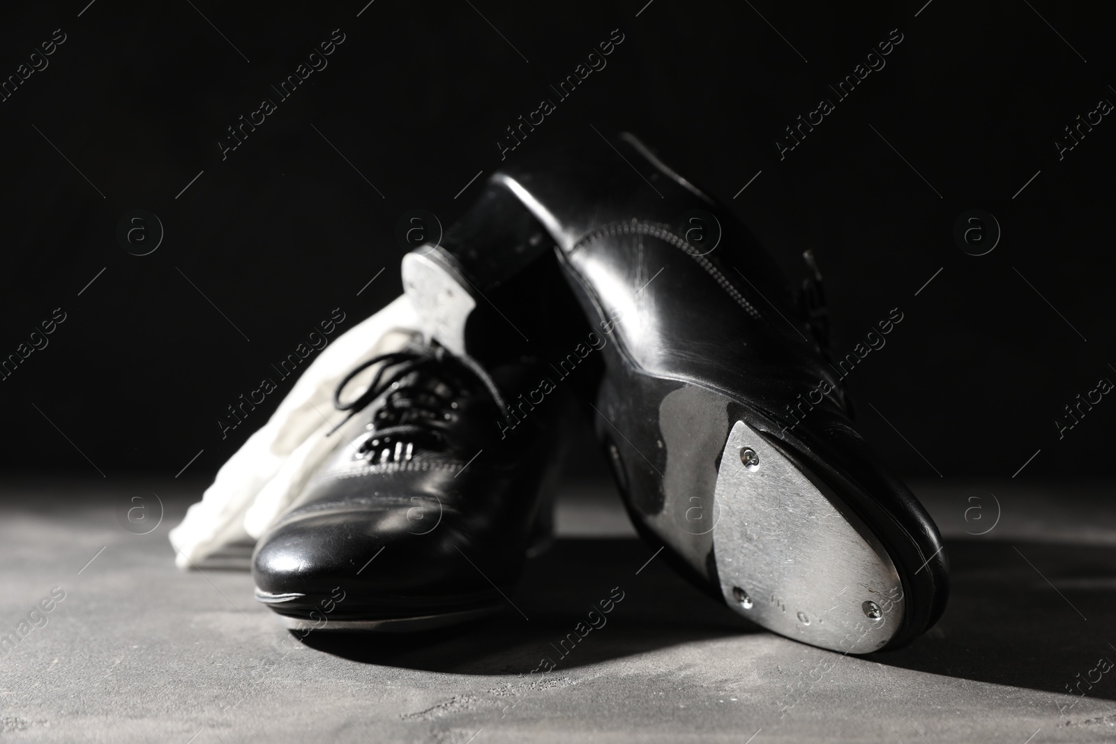 Photo of Pair of shoes for tap dance and white gloves on grey surface against black background, closeup