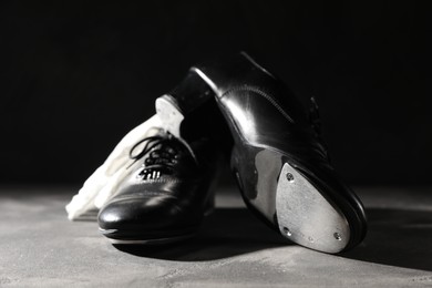 Photo of Pair of shoes for tap dance and white gloves on grey surface against black background, closeup