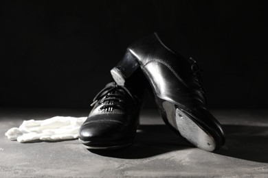 Photo of Pair of shoes for tap dance and white gloves on grey surface against black background, closeup