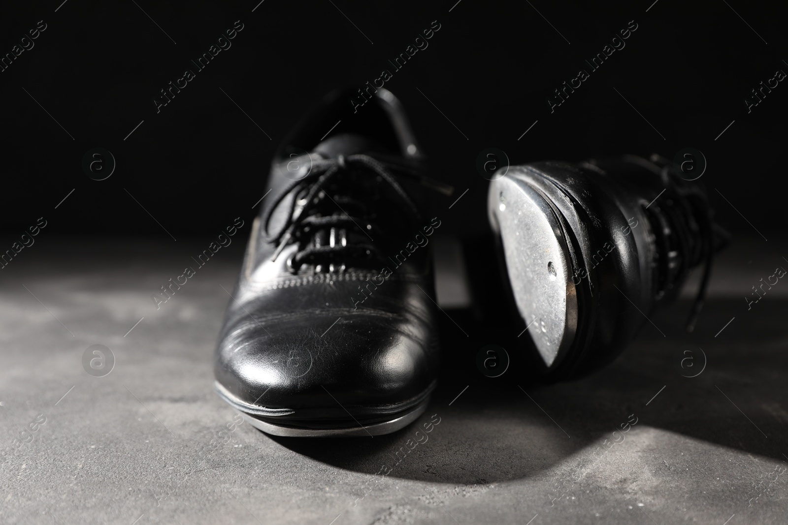 Photo of Pair of shoes for tap dance on grey surface against black background, closeup