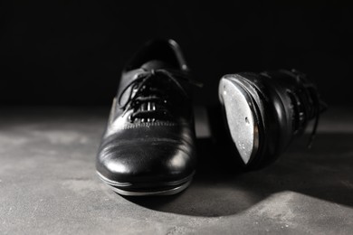 Photo of Pair of shoes for tap dance on grey surface against black background, closeup