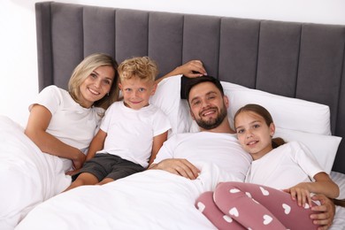 Photo of Family portrait of happy parents and their children on bed at home