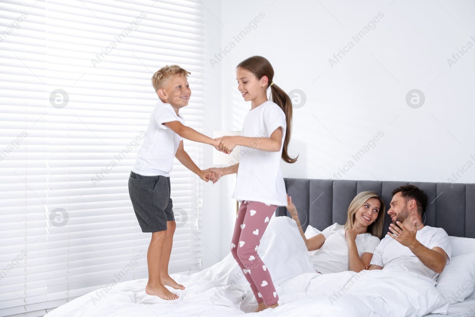 Photo of Happy parents lying in bed while their children jumping at home. Family
