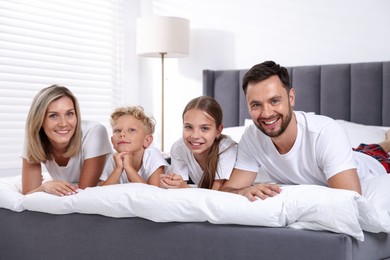 Photo of Family portrait of happy parents and their children on bed at home