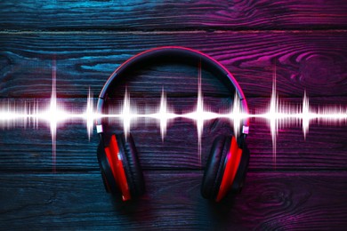 Image of Headphones on wooden background and sound waves, top view