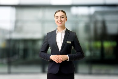 Image of Young hostess smiling near hotel. Space for text