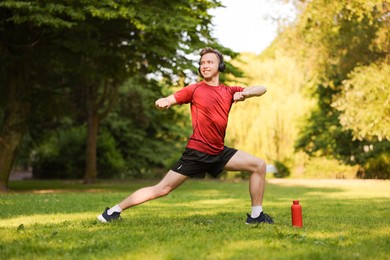 Photo of Smiling sportsman in headphones doing morning exercise outdoors