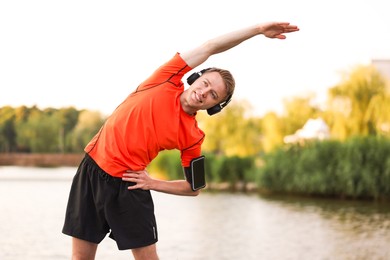 Photo of Smiling sportsman in headphones and armband doing morning exercise near river