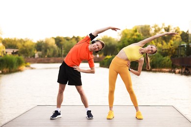 Photo of Smiling couple in headphones doing morning exercise on pier near river