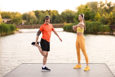 Photo of Smiling couple in headphones doing morning exercises on pier near river