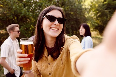 Photo of Young woman with beer taking selfie at party outdoors