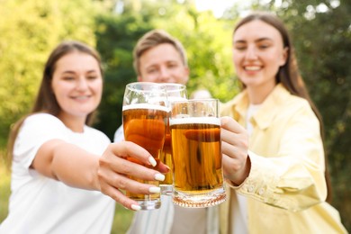 Photo of Group of happy friends clinking glasses of beer outdoors, selective focus