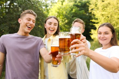 Photo of Group of happy friends clinking glasses of beer outdoors, selective focus
