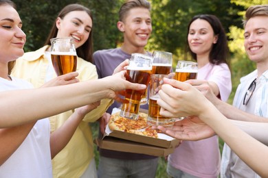 Photo of Group of happy friends with pizza clinking glasses of beer outdoors, selective focus