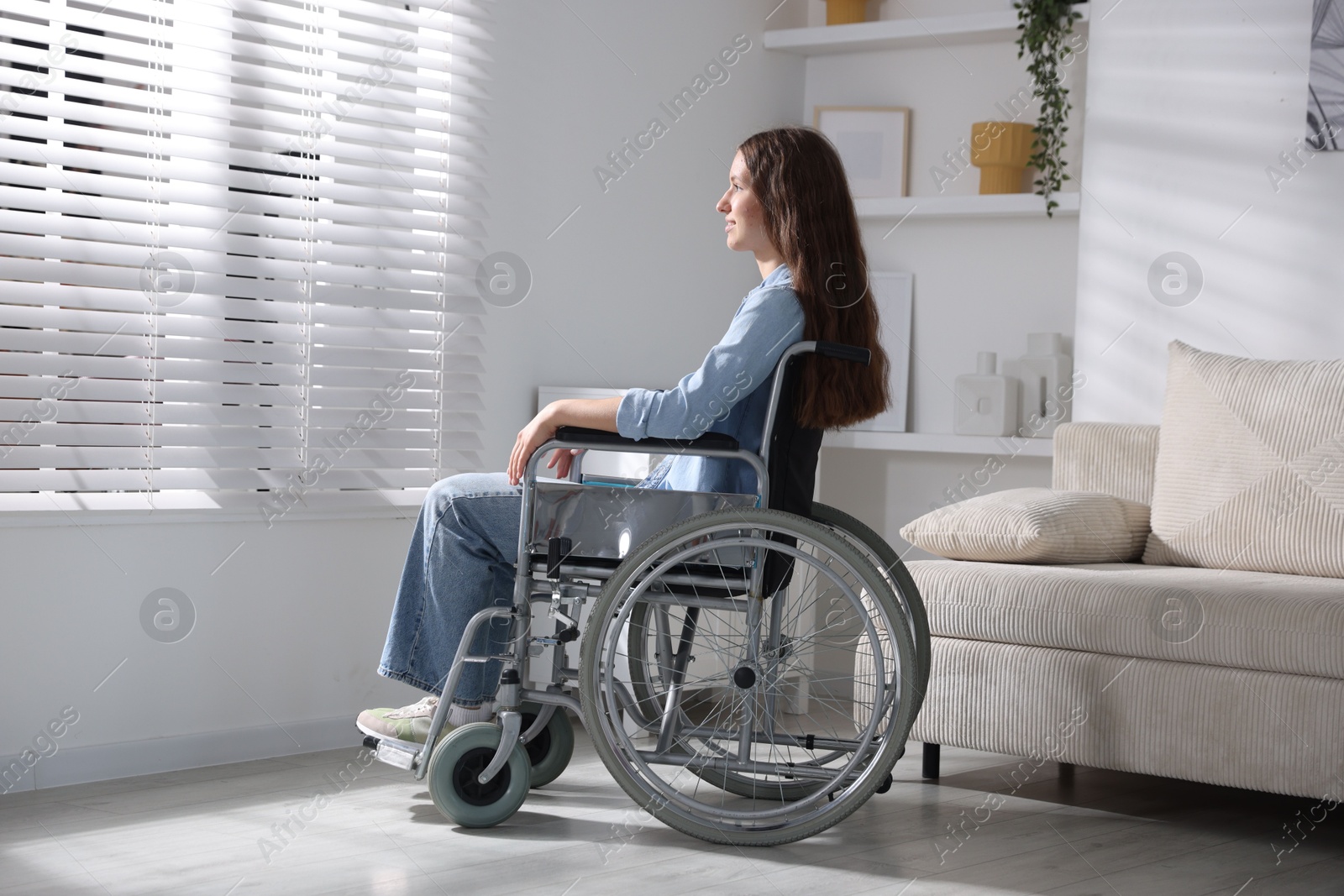 Photo of Beautiful teenage girl in wheelchair near window indoors