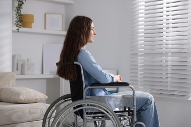 Photo of Beautiful teenage girl in wheelchair near window indoors