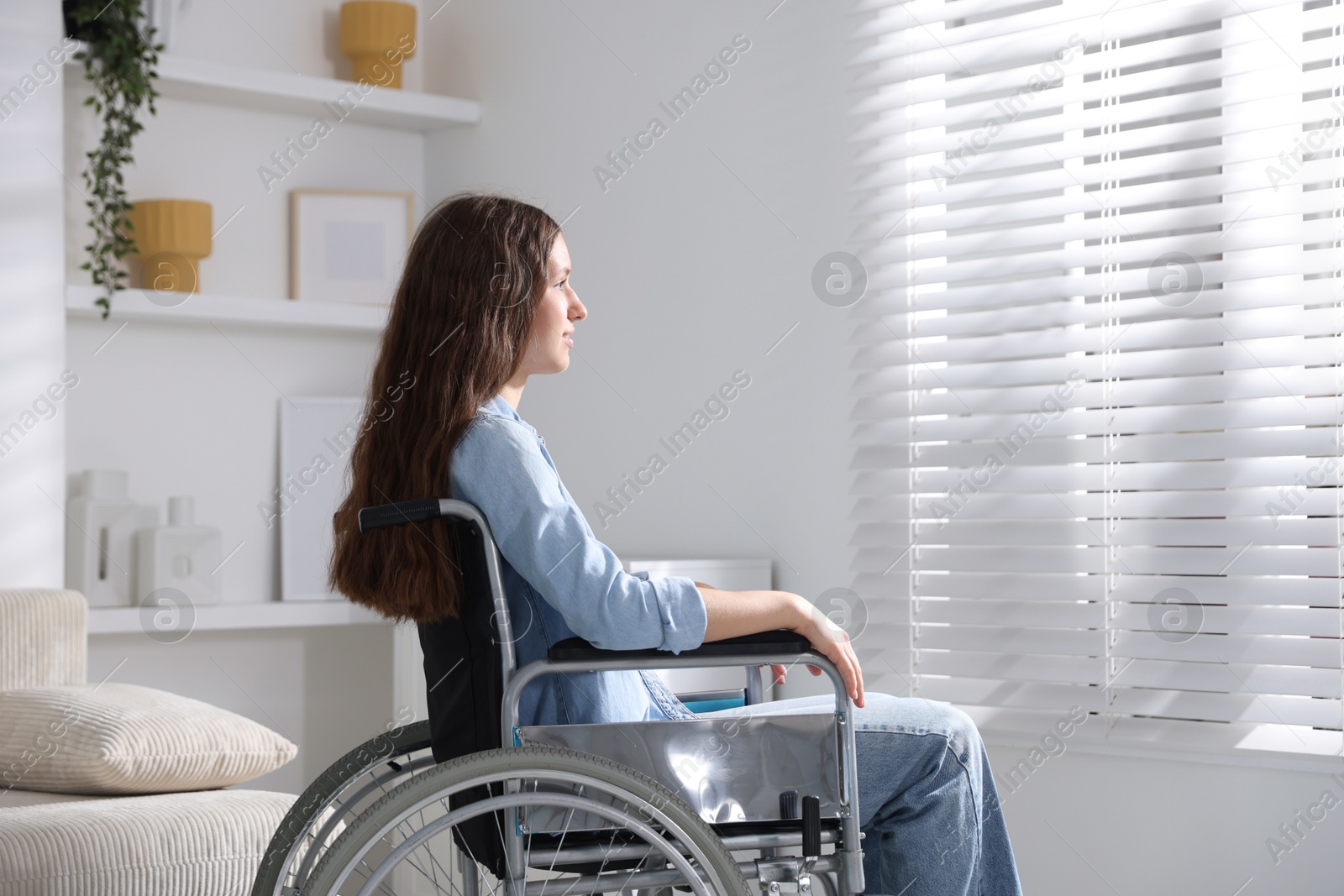 Photo of Beautiful teenage girl in wheelchair near window indoors
