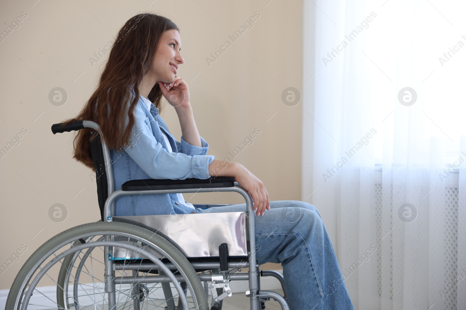 Photo of Smiling teenage girl in wheelchair near window indoors