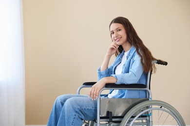 Photo of Smiling teenage girl in wheelchair near beige wall indoors