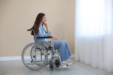 Photo of Beautiful teenage girl in wheelchair near window indoors