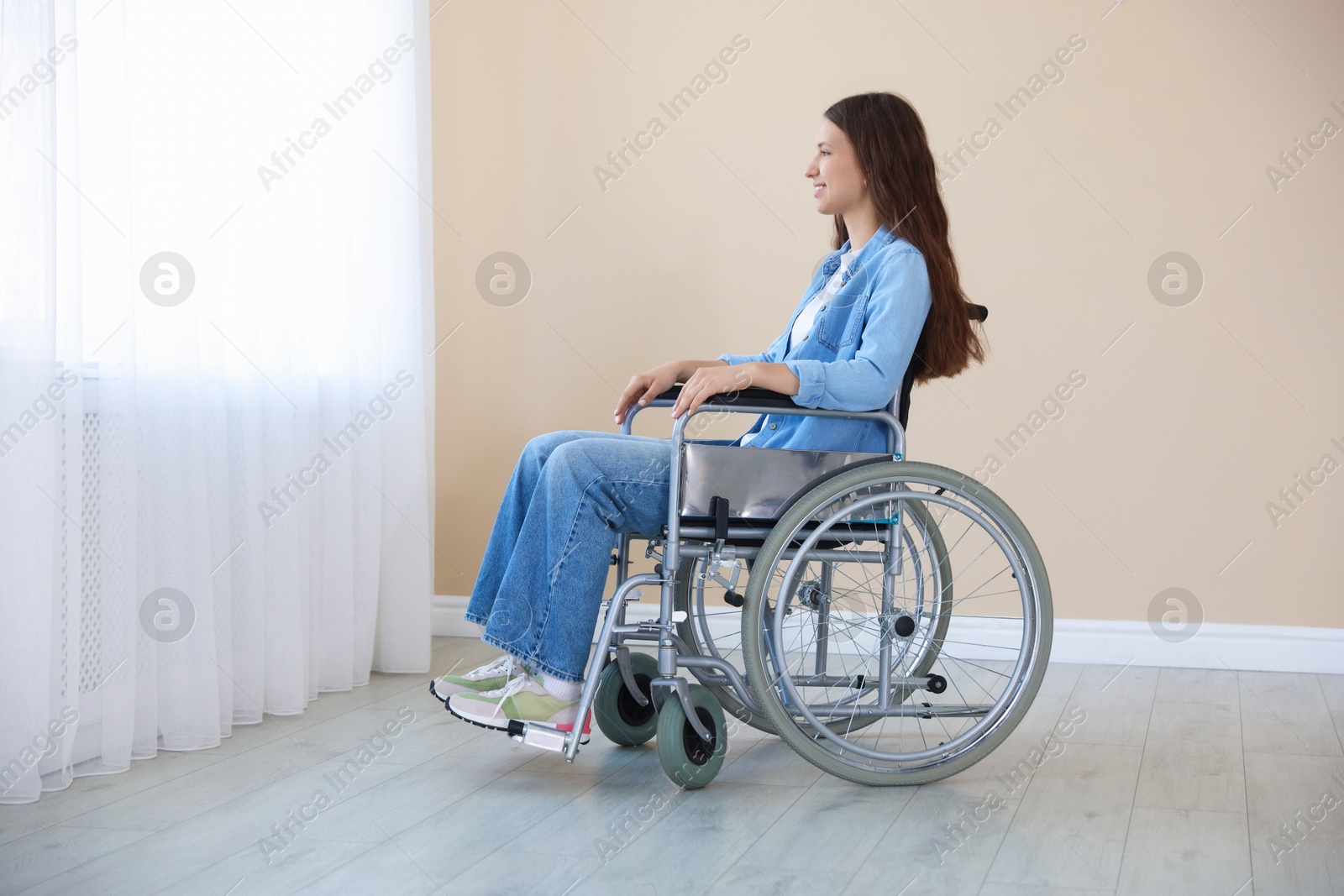 Photo of Smiling teenage girl in wheelchair near window indoors