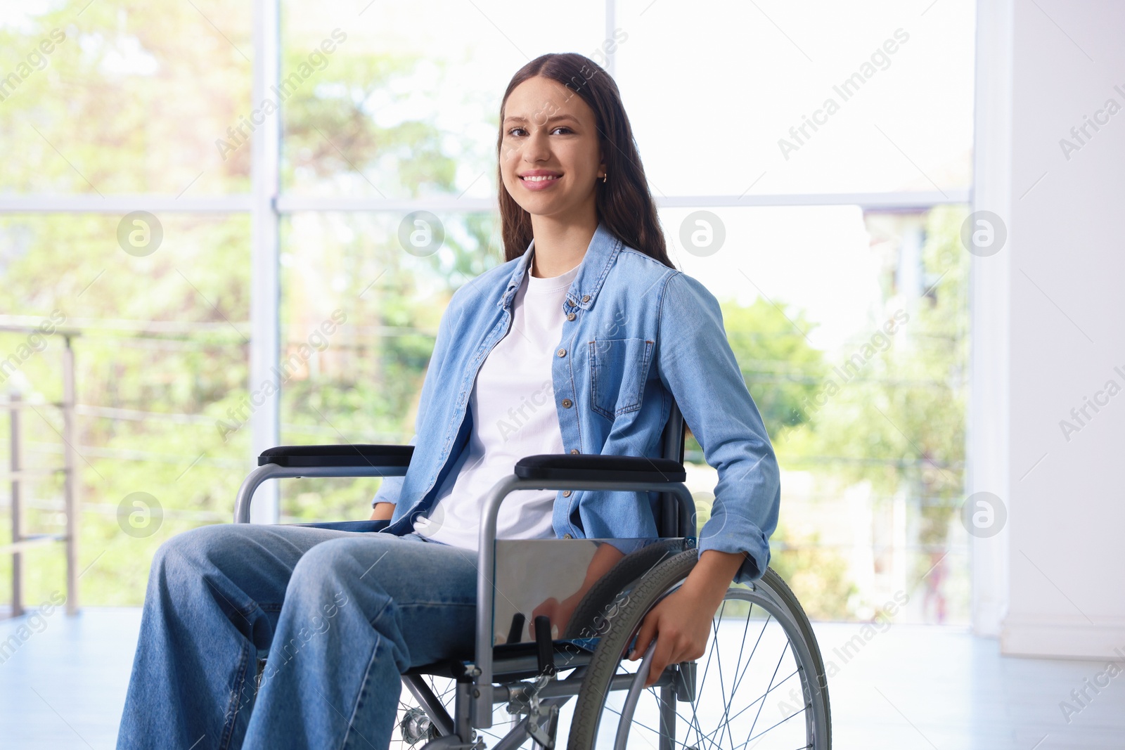 Photo of Smiling teenage girl in wheelchair near window indoors