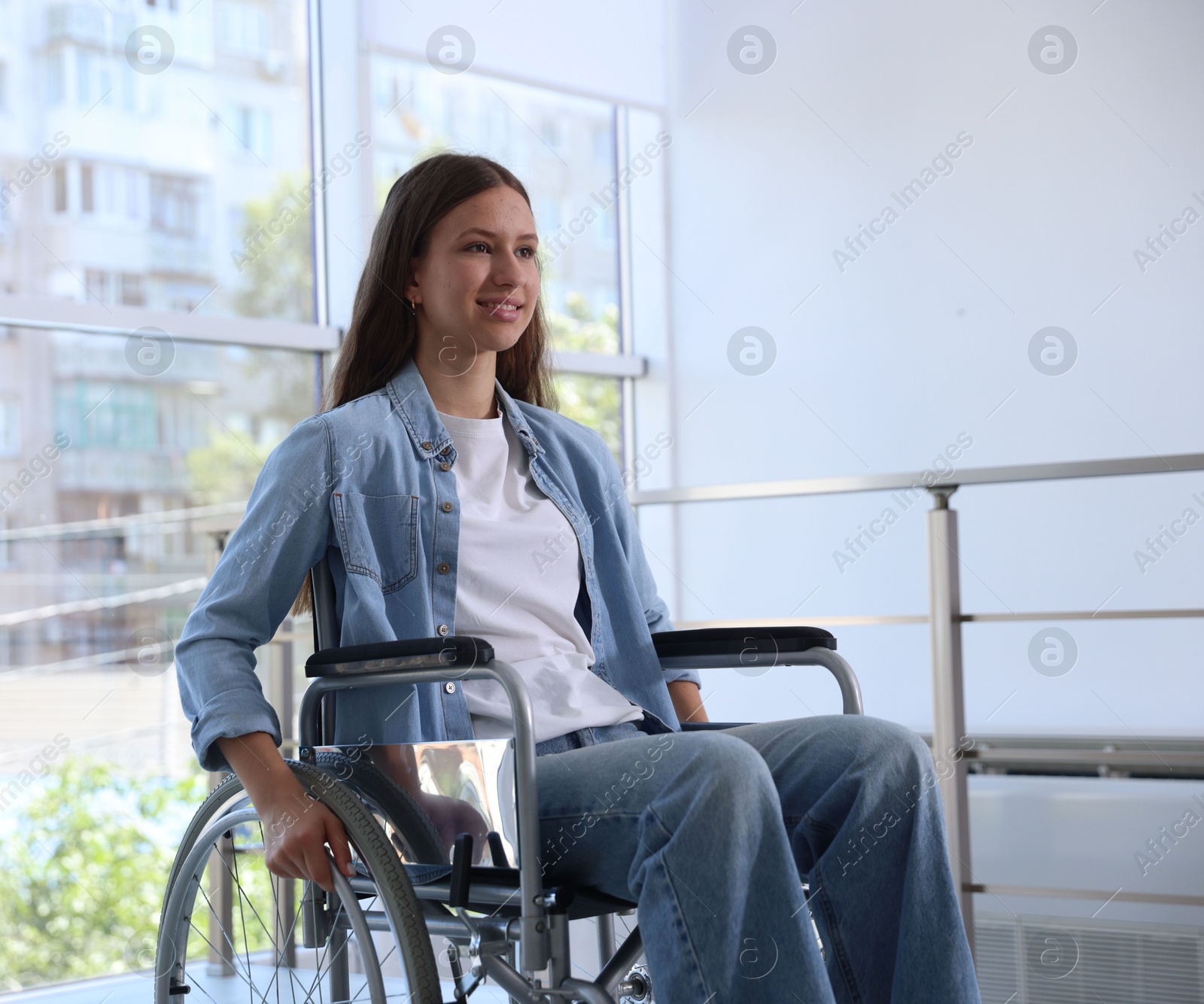 Photo of Smiling teenage girl in wheelchair near window indoors