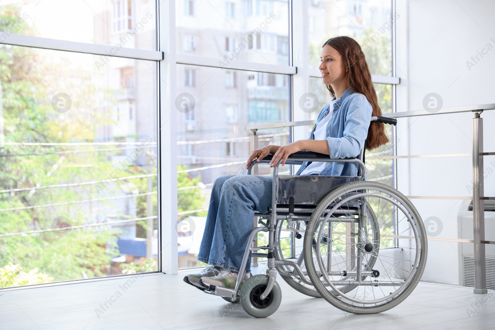 Photo of Smiling teenage girl in wheelchair near window indoors