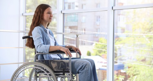 Photo of Beautiful teenage girl in wheelchair near window indoors