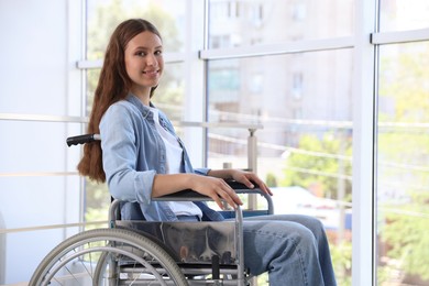 Photo of Smiling teenage girl in wheelchair near window indoors