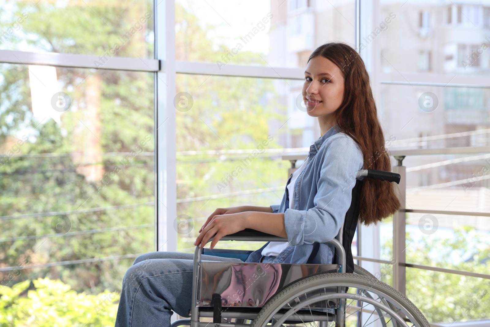 Photo of Smiling teenage girl in wheelchair near window indoors