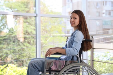 Photo of Smiling teenage girl in wheelchair near window indoors
