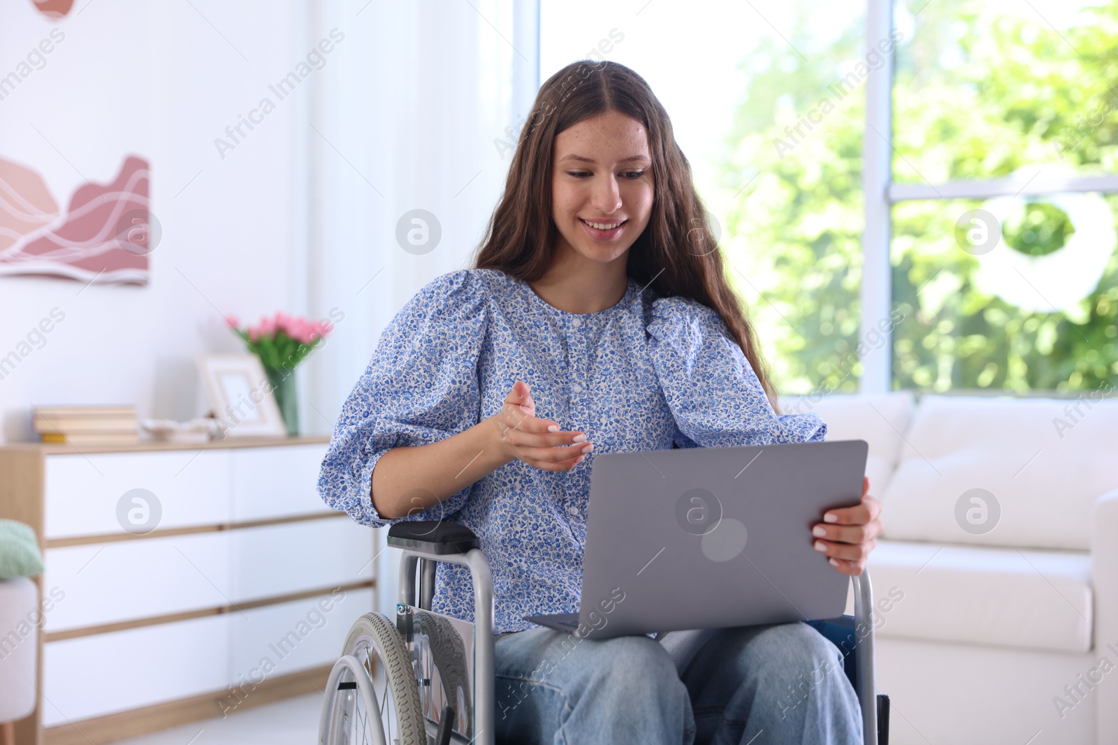 Photo of Smiling teenage girl in wheelchair having videochat by laptop at home