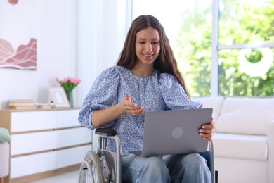 Photo of Smiling teenage girl in wheelchair having videochat by laptop at home