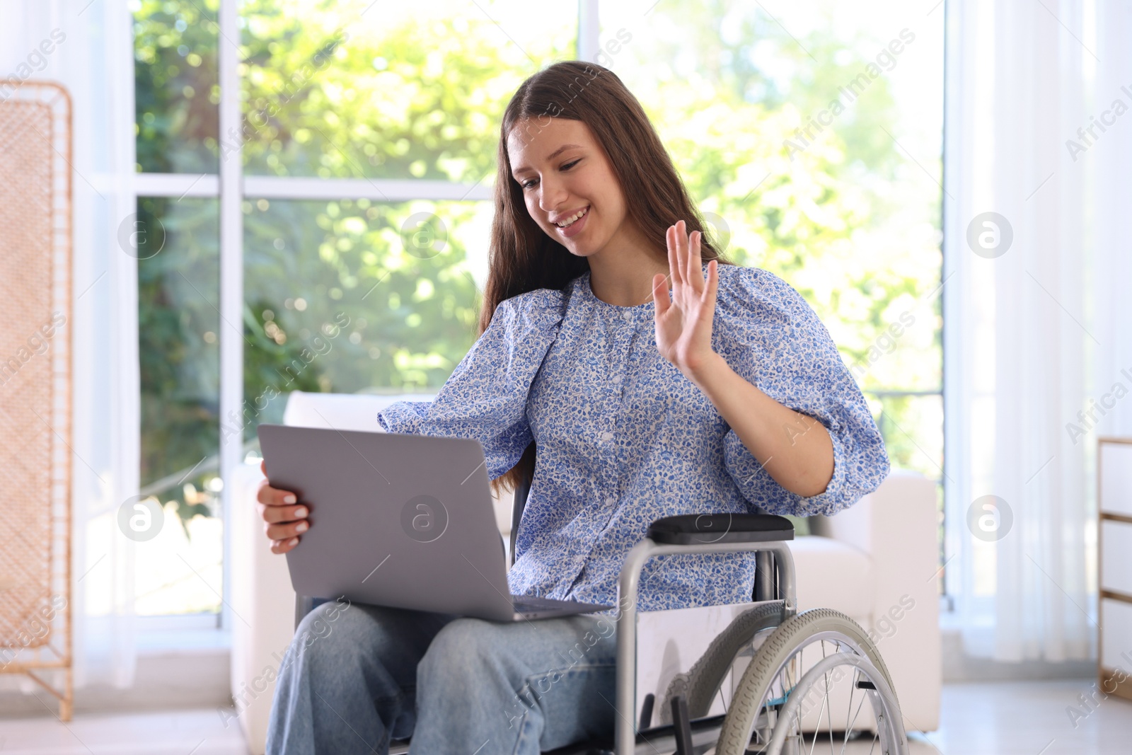 Photo of Smiling teenage girl in wheelchair having videochat by laptop at home