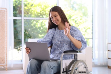 Photo of Smiling teenage girl in wheelchair having videochat by laptop at home