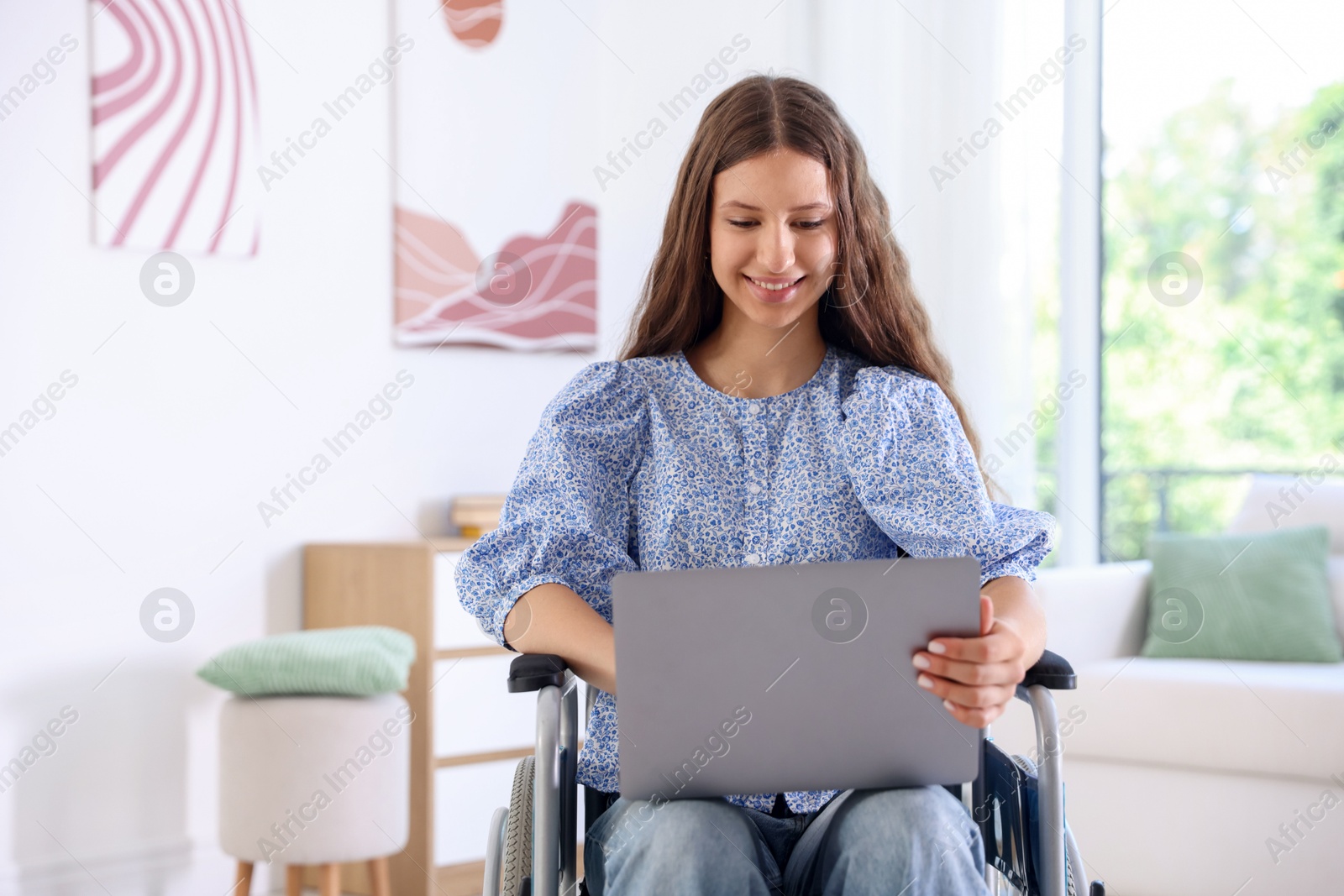 Photo of Smiling teenage girl in wheelchair using laptop at home
