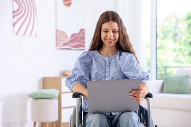 Photo of Smiling teenage girl in wheelchair using laptop at home