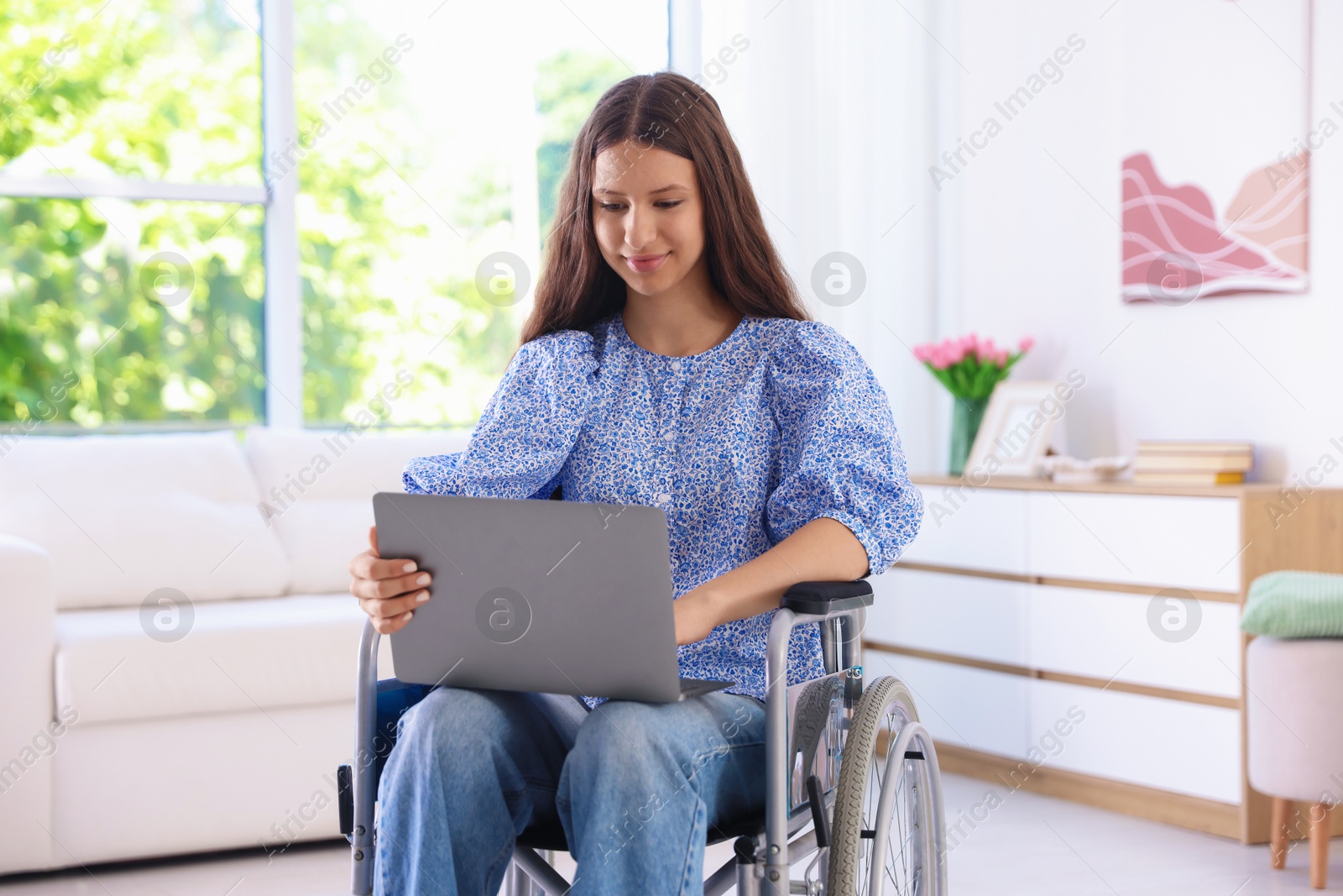 Photo of Beautiful teenage girl in wheelchair using laptop at home
