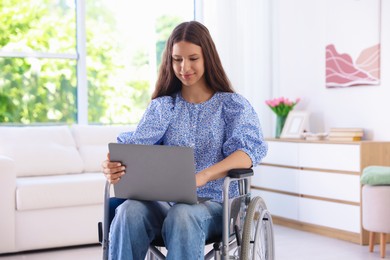 Photo of Beautiful teenage girl in wheelchair using laptop at home