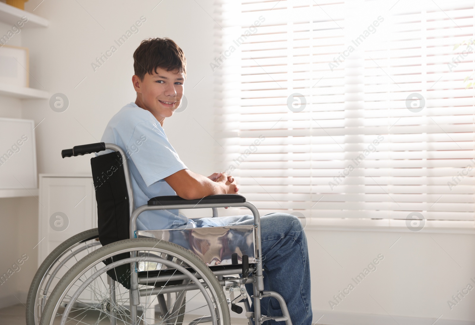 Photo of Happy teenage boy in modern wheelchair indoors, space for text