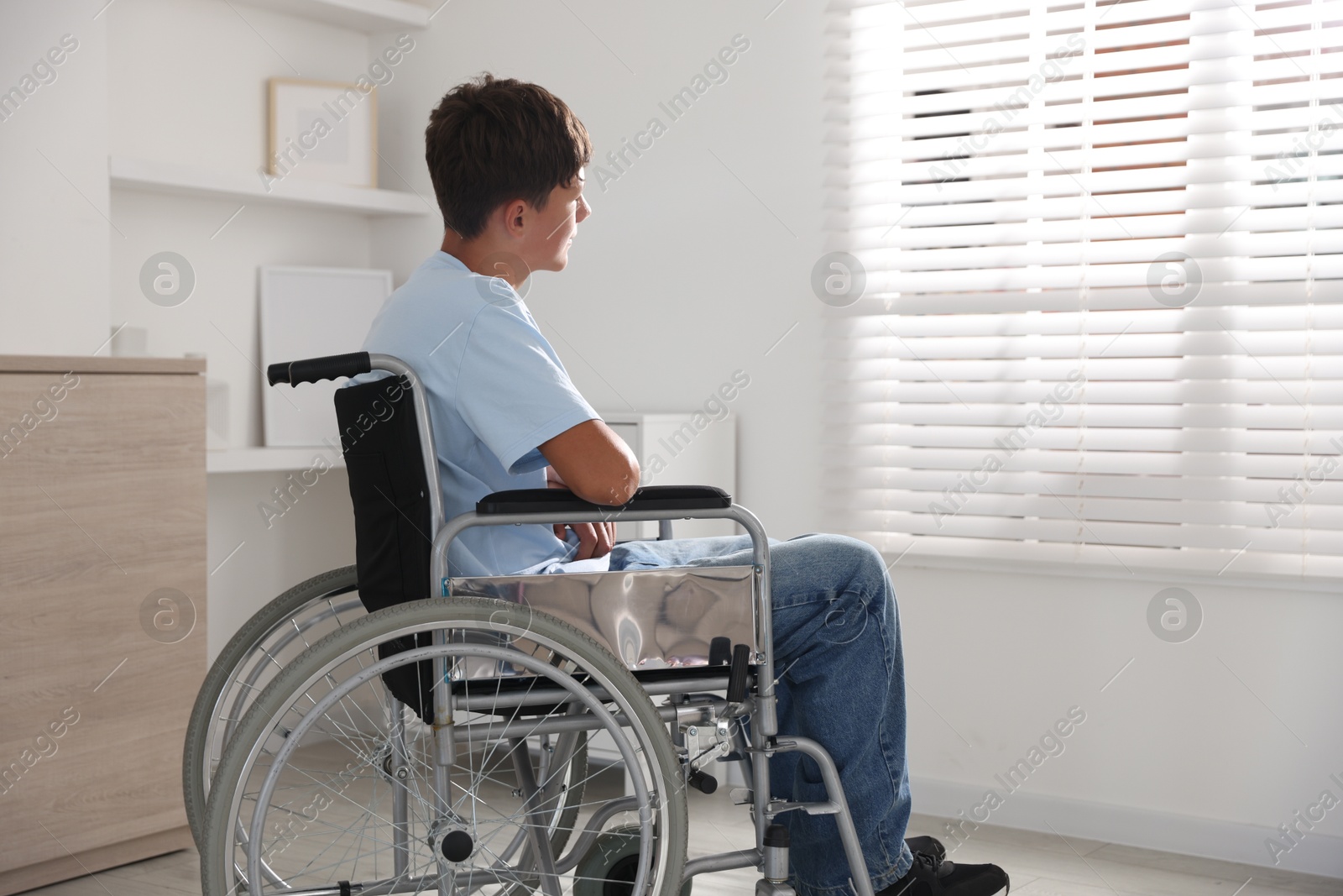 Photo of Teenage boy in modern wheelchair indoors, back view. Space for text