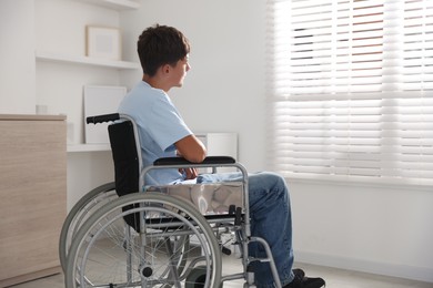 Photo of Teenage boy in modern wheelchair indoors, back view. Space for text