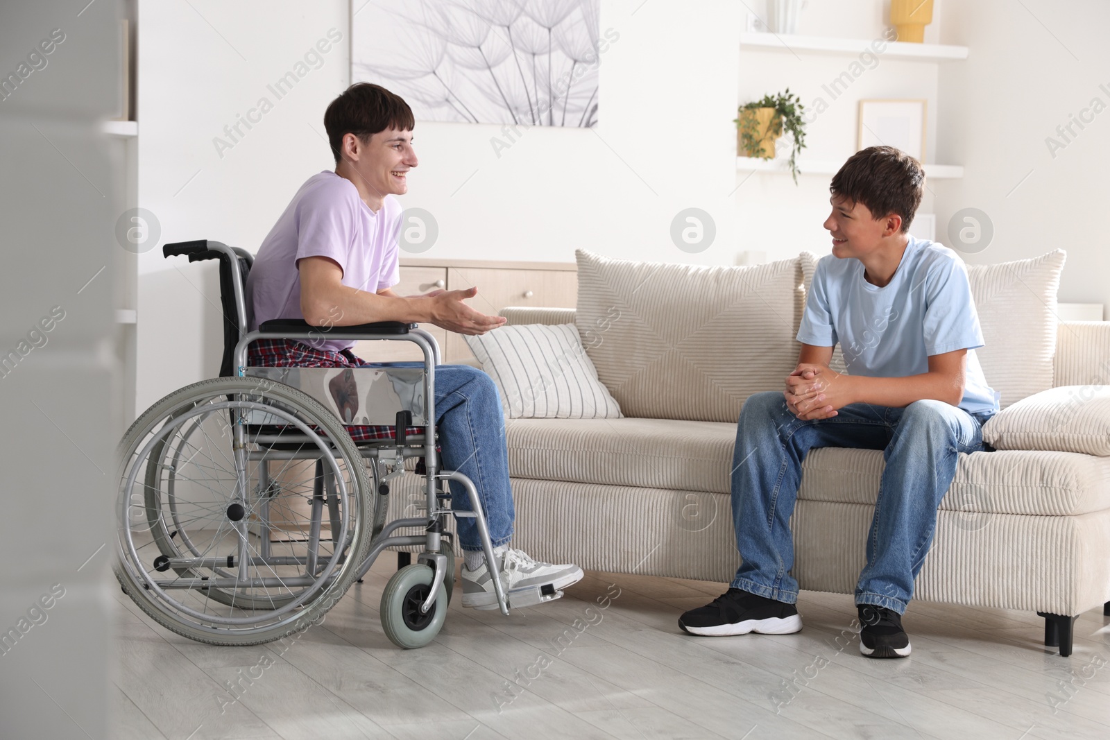 Photo of Happy young man in wheelchair and caregiver indoors