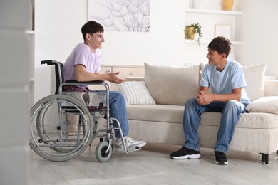 Photo of Happy young man in wheelchair and caregiver indoors