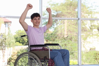 Photo of Happy young man in modern wheelchair indoors, space for text
