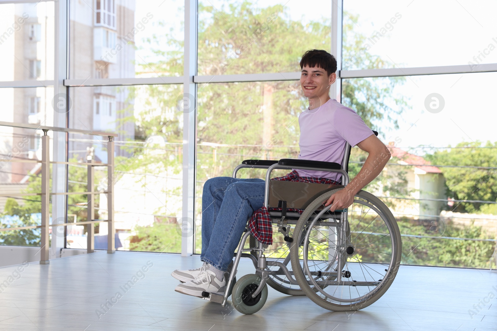 Photo of Happy young man in modern wheelchair indoors, space for text
