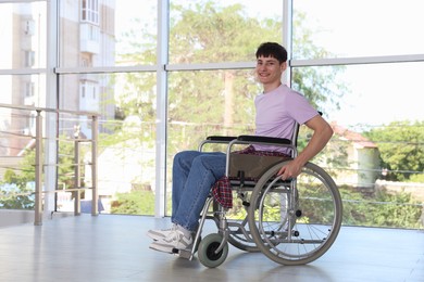 Photo of Happy young man in modern wheelchair indoors, space for text