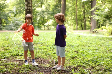 Photo of Cute little kids having fun with soap bubbles in park, space for text