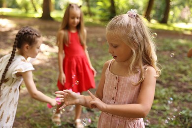 Photo of Cute little kids having fun with soap bubbles in park, selective focus
